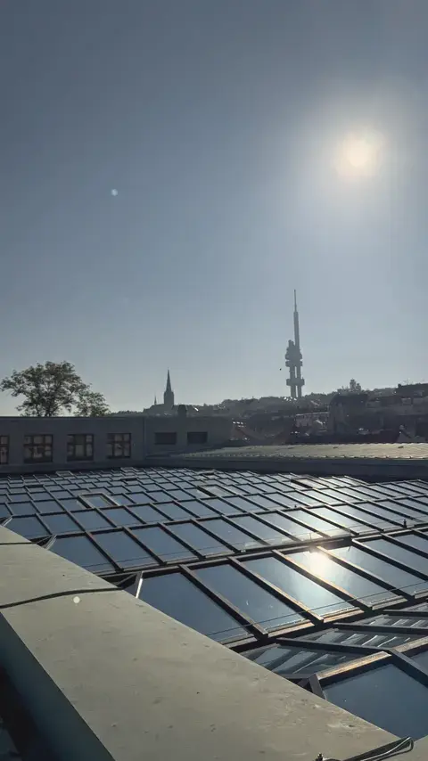 頂樓的玻璃天窗反射著太陽，遠方是 Žižkov 電視塔。