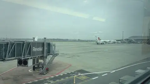 空橋伸向停機坪，遠處一架飛機正在滑行。